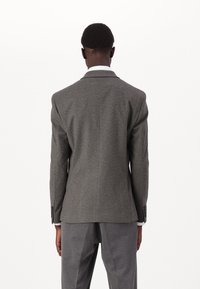 Grå ullblazer med strukturerade axlar, notched laplar och slim fit. Har två bakventiler och knäppte manschetter. Bärs med grå byxor.