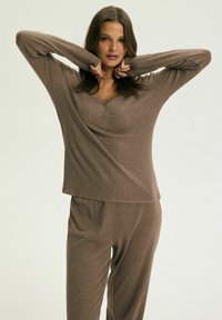 Brązowa bluzka z długim rękawem w serek z detalami w postaci guzików, zestawiona z pasującymi brązowymi spodniami; luźny krój, miękka tkanina i ribbowa struktura.