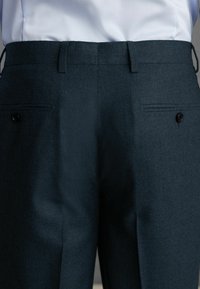 Ciemnozielone spodnie z teksturowanej tkaniny, slim fit, z dwoma tylnymi kieszeniami i czarnymi guzikami. Odpowiednie do formalnych strojów.