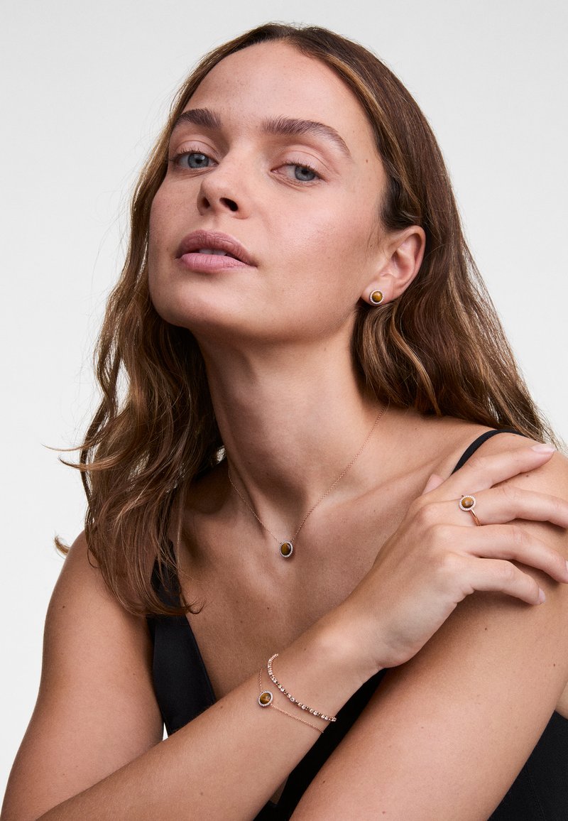 Arany tónusú ékszerszett, amely egy medálos nyakláncból, fülbevalóból és gyűrűből áll, mindegyik középpontjában sötét kővel és finom részletekkel.