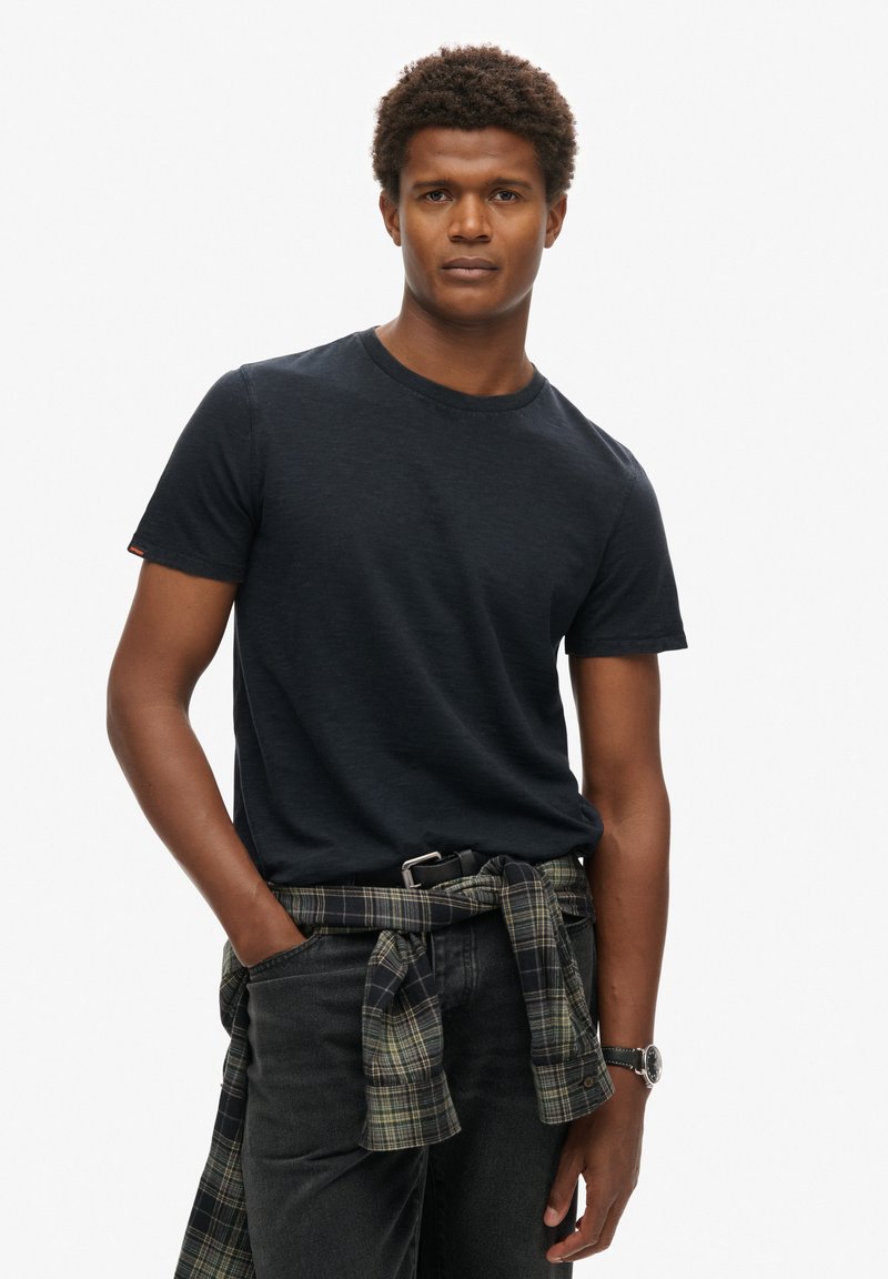 T-shirt nera a maniche corte realizzata in un tessuto testurizzato. Abbinata a jeans scuri e una camicia a quadri annodata in vita.