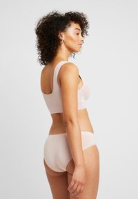 Lys rosa bralette og matchende truse i elastisk stoff. Glatt tekstur, brede stropper på toppen, og høy midje-kutt nederst.