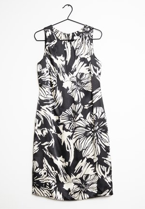 Černé šaty bez rukávů s velkými bílými květinovými a abstraktními vzory visící na černém ramínku na bílém pozadí.