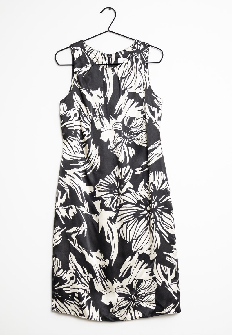 Robe noire sans manches avec de grands motifs floraux blancs et des motifs abstraits, suspendue sur un cintre noir contre un fond blanc.