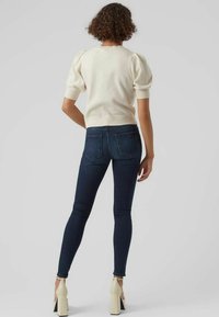 Krämpuff-sleeve tröja i kombination med mörkblå slim-fit jeans, med en slät yta och minimalistisk design på bakfickorna. Beigefärgade högklackade skor.