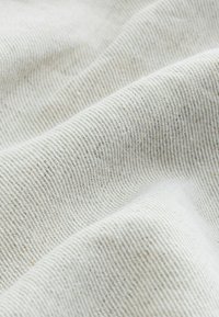 Gros plan d’un tissu côtelé doux de couleur beige clair avec un motif de tissage visible et des plis légers créant une surface texturée.