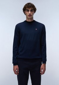 Marineblaues Langarmpullover mit Rundhalsausschnitt und gerippten Bündchen. Hat ein kleines rot-weißes Logo auf der linken Brust.