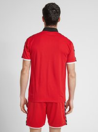 Röd sportpolo med svart krage, med korta ärmar och vitt trim. Bärs med matchande röda shorts som visar en slank atletisk design.