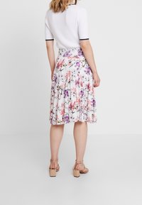 Gonna plissettata floreale bianca con fiori rosa e viola, abbinata a un top bianco a costine. Sandali con tacco a blocco color cammello completano il look.