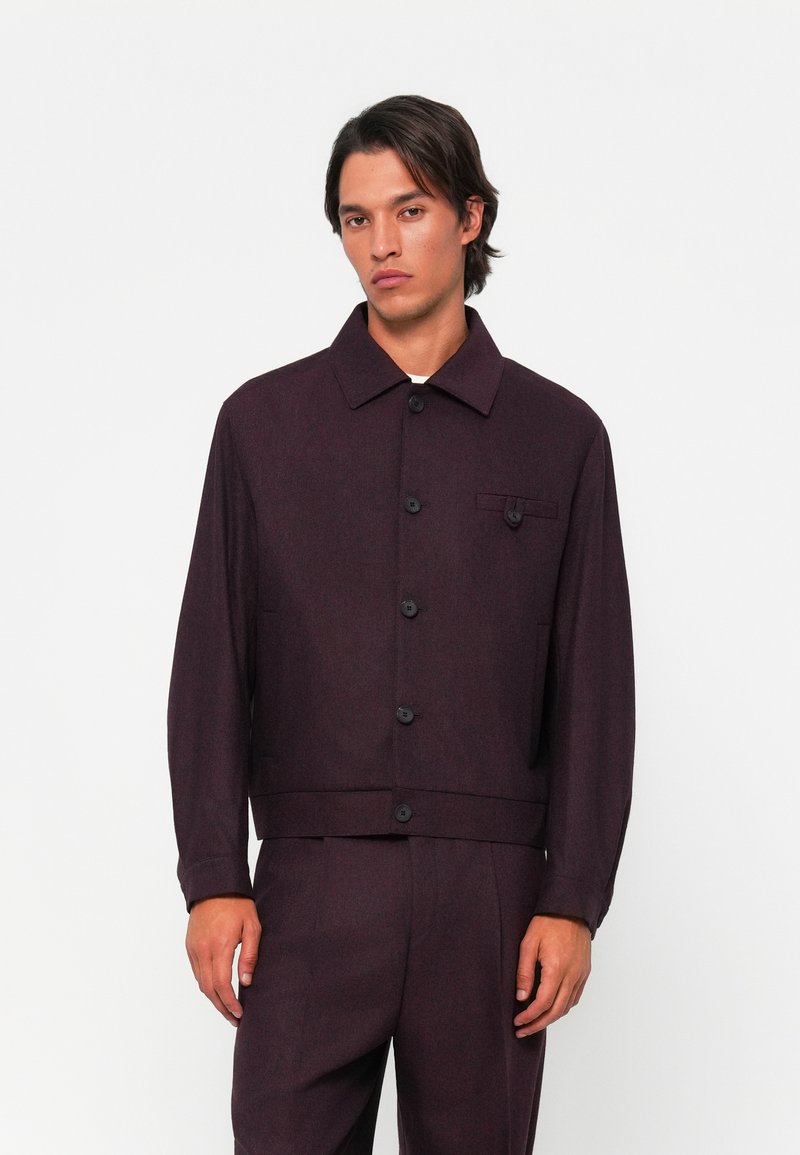 Burgundy jacket made of textured fabric, featuring a collar, front buttons, and a chest pocket with a flap. Long sleeves and straight fit.