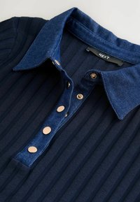 Marinblus med ribbat mönster, denimkrage och knapplist, prydd med gyllene knappdetaljer. Tyget har en slät textur och vertikala ränder.