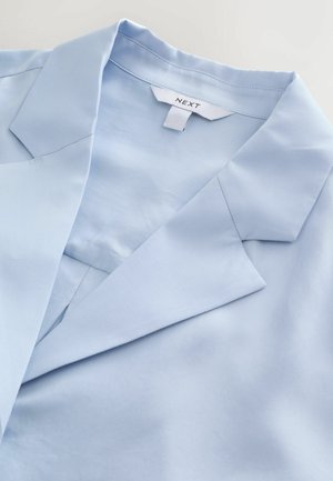 Šviesiai mėlynas, lygus audinys su įpjauta apykakle ir apykaklės stovu. Drabužis pasižymi švelniu blizgesiu, atskleidžiančiu jo struktūruotą, bet laisvą dizainą.