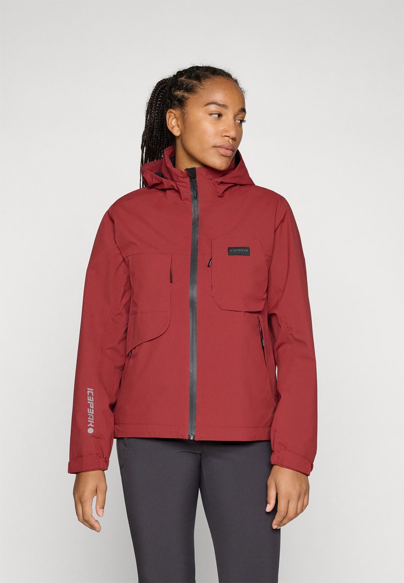 Red waterproof jacket with a zip front, two chest pockets, adjustable hood, and elastic cuffs. Features logo on the left arm.