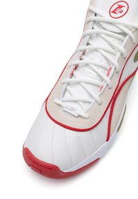 Valge nahast tennis, millel on punased ja kullased aksendid, sile tekstuur, perforatsioonidega paneelid ja valged paelad. Ümmargune varba disain.