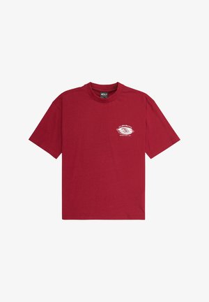 Czerwona bawełniana koszulka z małym białym nadrukiem na piersi, w połączeniu z luźnymi turkusowymi spodniami z sztruksu i czarnymi trampkami.