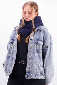 Light blue denim jacket with oversized fit and button closure, paired with a thick, navy knitted scarf. Black top and pants complete the outfit.