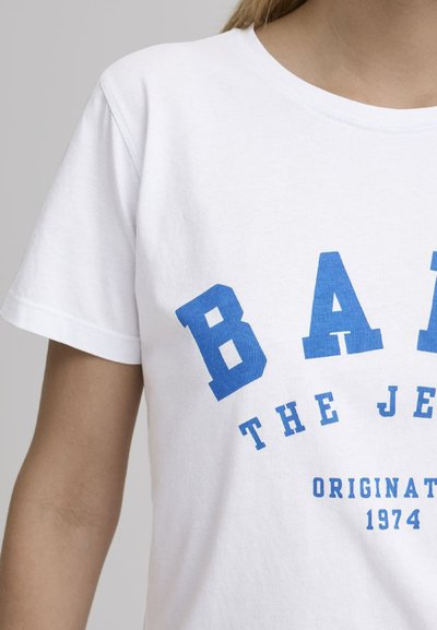 Hvit bomull t-skjorte med fet blå tekst som sier "BAND THE JET" med "ORIGINAL 1974" under. Standard rund hals og korte ermer.