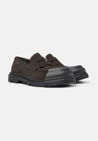 Zapatos tipo slip-on de ante marrón oscuro con una gruesa puntera de goma negra, costuras de contraste y una suela texturizada resistente. Sin marcas visibles.