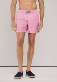 Różowe spodenki kąpielowe z małym geometrycznym wzorem, elastyczny pas z sznurkiem do regulacji oraz cięcie do połowy uda. W zestawieniu z granatowymi zamszowymi butami wsuwanymi.