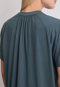 Dunkelblaues T-Shirt mit rundem Ausschnitt und gerafftem Detail auf der Rückseite, aus weichem, leichtem Stoff mit kurzen Ärmeln.