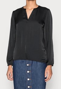 Svart blus med långa ärmar i slätt material, med V-ringning och samlade manschetter, tillsammans med en denimkjol med knappar framtill.