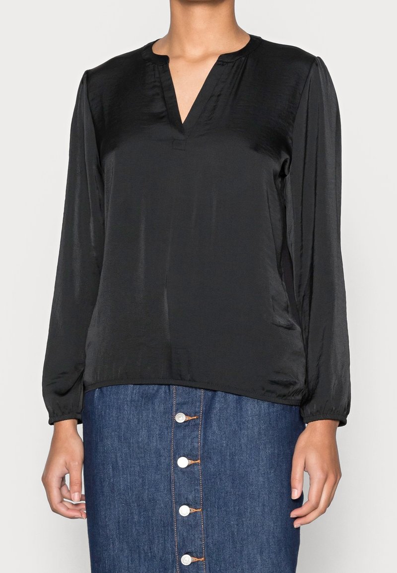 Svart blus med långa ärmar i slätt material, med V-ringning och samlade manschetter, tillsammans med en denimkjol med knappar framtill.