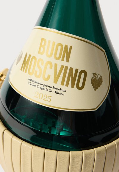 Grøn glasflaske med en tapet form og en tekstureret beige bund. Etiketten har guldtekst og læser "BUON MOSCINO 2025."