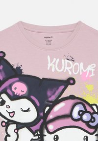 Różowy bawełniany t-shirt z graficznym wzorem postaci w odcieniach fioletu, czerni i bieli. Napis "KUROMI" ze szczegółami w formie rozprysków.