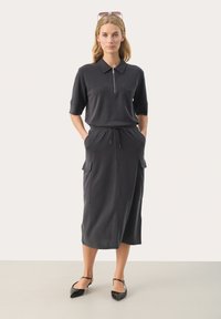 Donkergrijze polodress met een rits aan de voorkant, korte mouwen, een aantrekkoord in de taille en twee zijzakken. Glad van textuur en met een lengte tot halverwege de kuit.
