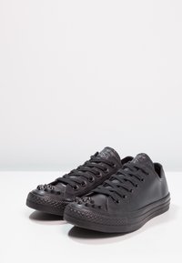 Black leather low-top sneakers with rubber soles, featuring spike accents on the toe, flat laces, and a textured side panel.