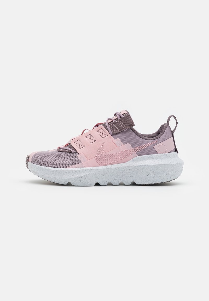 Zapatilla deportiva en tonos morados y rosas con un diseño de malla texturizada, correas reforzadas y una gruesa suela blanca moteada con un patrón de olas.