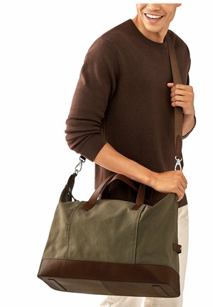 Sac de voyage en toile khaki avec des accents en cuir brun, doté de deux poignées supérieures et d'une bandoulière détachable, texture lisse et forme rectangulaire.