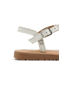 Sandalia de cuero blanca con una correa delgada, hebilla plateada ajustable y suela de goma marrón con un patrón de agarre texturizado.