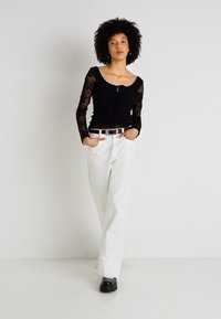 Μαύρη μπλούζα με μακριά μανίκια και δαντέλα, σε συνδυασμό με λευκά παντελόνια και λευκή ζώνη. Μαύρα υποδήματα ολοκληρώνουν το ντύσιμο.