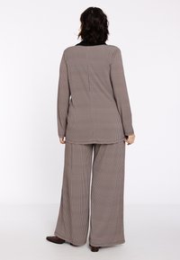 Twee-delige outfit met een geruit patroon in gedempte bruintinten. De blazer heeft een zwarte kraag en de wijde broek valt soepel.