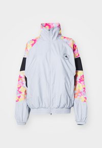 Chaqueta cortavientos de color gris claro con mangas de tie-dye coloridas en rosa, amarillo y naranja, con un cuello alto y puños elásticos.