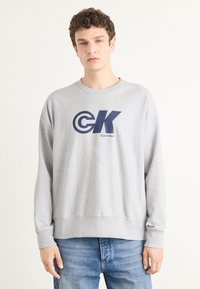 Šedá mikina vyrobená z bavlněné směsi, s velkým námořnickým logem "CK" a textem "Calvin Klein". Měkká textura, žebrované manžety a lem.