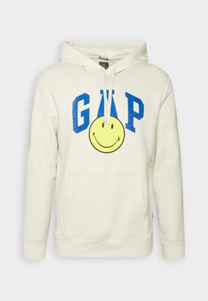 Kremowa bluza z kapturem wykonana z bawełny, z przednią kieszenią, białymi sznurkami ściągającymi, niebieskim napisem GAP i dużą grafiką żółtej uśmiechniętej buźki.