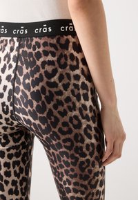 Leggings met luipaardprint, voorzien van een zwarte elastische tailleband met de merknaam "crās," met een aansluitend ontwerp en een gladde textuur.