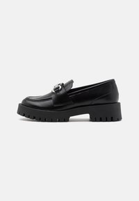 Sorte skinnloafers med en kraftig, riftete såle og en metallisk spenneaksel på stroppen. Glatt tekstur, klassisk design.