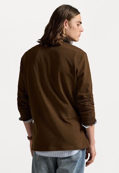 Bruine langemouwen shirt met een ontspannen pasvorm, zachte textuur en opgerolde mouwen over een lichtblauw en wit gestreept shirt. Achteraanzicht getoond.
