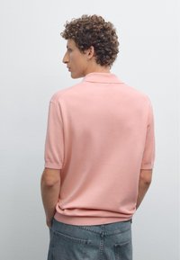 Ljusrosa kortärmad polo med en klassisk krage, tillverkad av mjukt material, i kombination med ljusgrå, avkopplande jeans.
