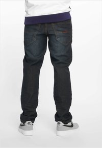 Mørkeblå denimjeans med en avslappet passform, synlig søm og to baklommer. Kombinert med grå og hvite Nike-sneakers.