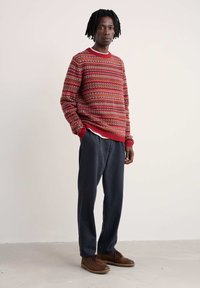 Sarkans džemperis ar ģeometriskām apdrukām, ar ribot�ām piedurknēm un kaklu. Valkāts ar tumši pelēkiem biksēm un brūnām šņorējamām kurpēm.