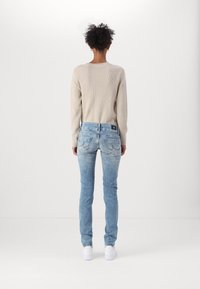 Light beige ribbed sweater paired with blue skinny jeans, featuring back pockets and a black tag. Model wears white sneakers.