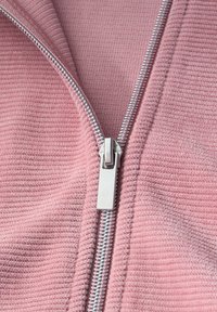 Sølv lynlås delvist åbnet på pink tekstureret stof, der viser fint strikket materiale og skinnende metal lynlås tænder.