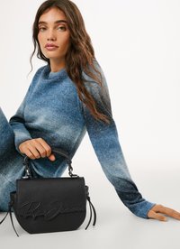 Bolso de mano de cuero negro con logo en relieve, forma redondeada, diseño estructurado y asa corta. La modelo lleva un suéter con degradado azul.
