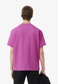 T-shirt di cotone rosa con maniche corte e colletto classico. Presenta un piccolo logo verde sopra il scollo e una vestibilità comoda.