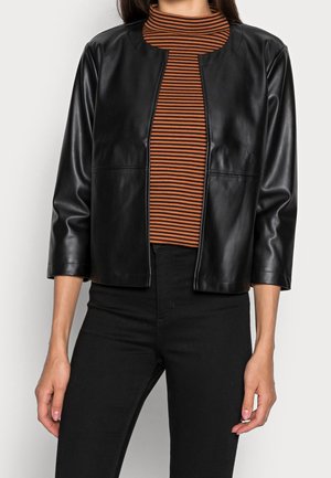 Kobieta w czarnej skórzanej otwartej kurtce na brązowym i czarnym paskowanym golfie oraz czarnych spodniach z wysokim stanem.