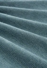 Textilstoff mit weicher, glatter Textur und einem subtilen blau-grauen Farbton; zeigt diagonale Falten und ein durchgehend gewebtes Muster.